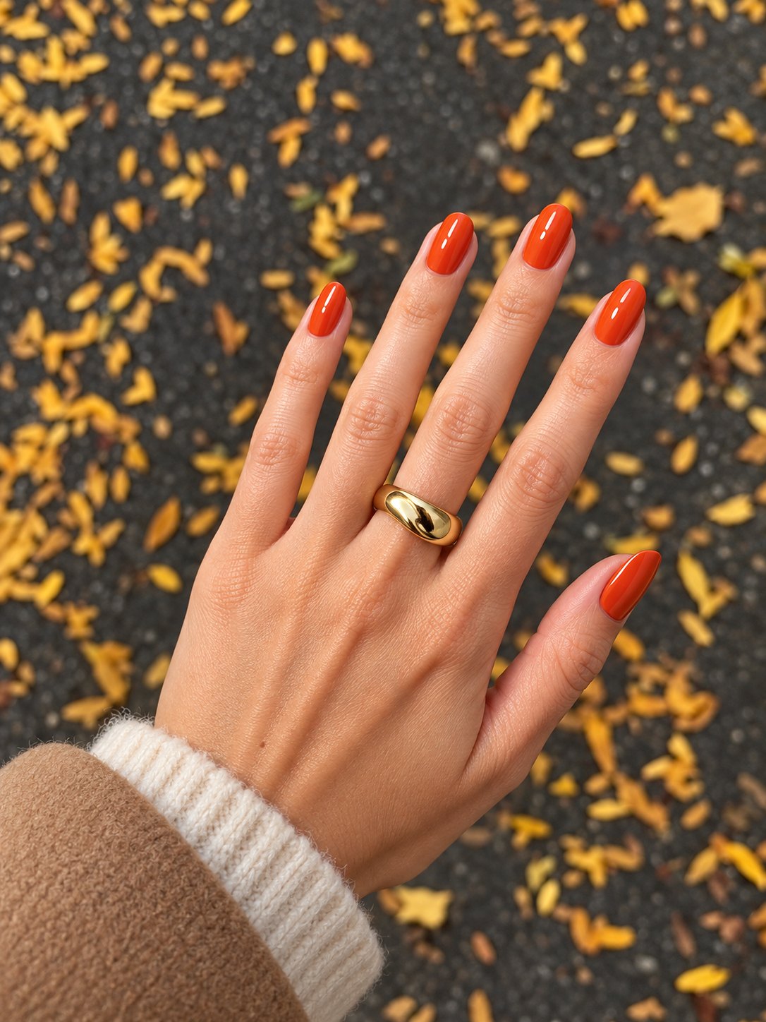 Main avec manucure gel orange automne 1944 Paris sur fond de feuilles mortes